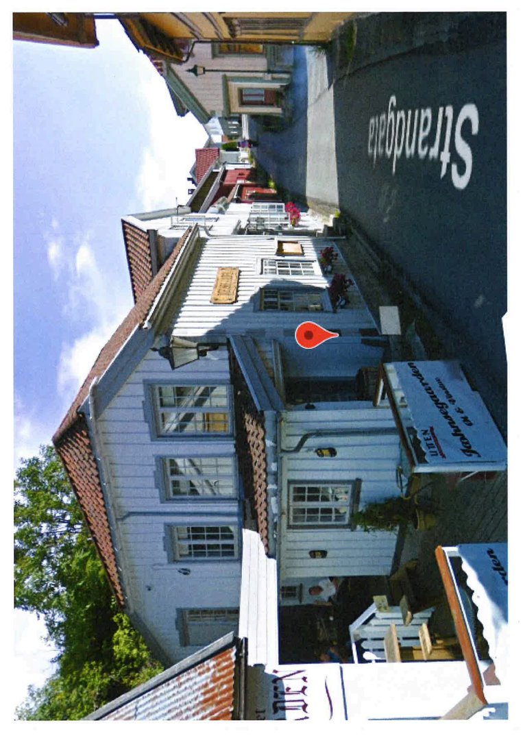 Fotografi av en eksisterende bygning (hvit, trepanel) sett fra gaten (Strandgata).