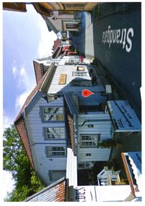 Fotografi av en eksisterende bygning (hvit, trepanel) sett fra gaten (Strandgata).