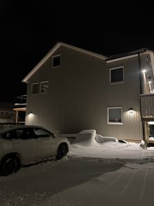 Fotografi av en bygning sett fra siden ved siden av en snødekket bil, tatt om natten.