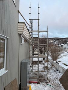 Fotografi av en bygning med en stor stige (scaffolding) oppstilt langs fasaden, sannsynligvis under en utvendig renovering eller vedlikehold.