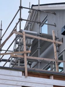 Fotografi av en bygning under oppføring eller renovering, med utvendig stålrekkverk (scaffolding) og trebjelker.
