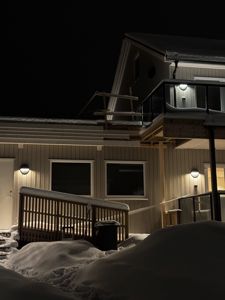Fotografi av en bygning sett fra siden, med snø på tak og terrasser, tatt om natten.