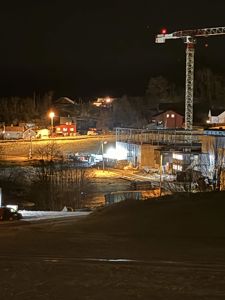 Fotografi av et byggeplass ved nattelys med en kran og en delvis ferdig bygning.