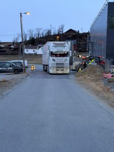 Fotografi av en byggeplass med en lastebil, en gaffeltruck og en delvis ferdig bygning i bakgrunnen.
