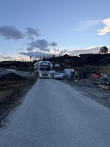 Fotografi av en byggeplass med en vei, kjøretøy og arbeidere.