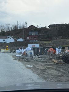 Fotografi av et byggeplassområde med materialer, containere og nabolag i bakgrunnen.