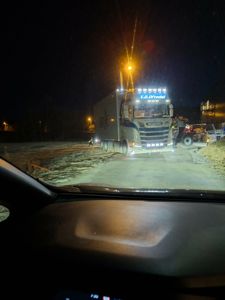 Fotografi tatt fra bilens fører sete som viser en lastebil på en vei ved et byggeplass eller anleggsområde om natten.