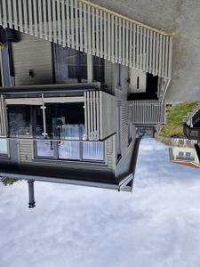 Fotografi av en moderne, toetasjes bolig med fasade av trepanel, balkonger og en hvit hekk i forgrunnen.