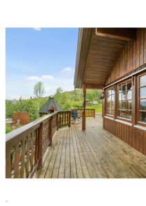 Fotografi av en uteplass med tredekk og -railing foran en hytte, sett fra innsiden eller kanten av verandaen.