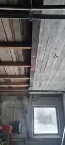 Fotografi av en ufullført eller under oppussing bygning, som viser takkonstruksjon med trebjelker og gipsplater.