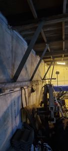 Fotografi av en byggeplass eller et underbyggingsarbeid, som viser stålbjelker festet til en betongvegg og diverse byggematerialer.