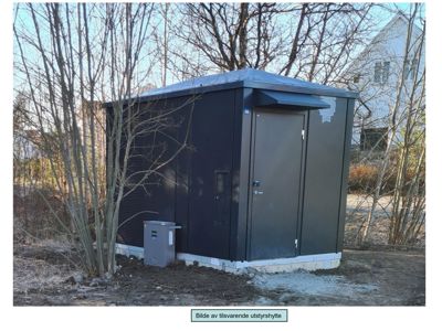 Fotografi av en ferdig installert, mørk utstyrshytte (sannsynligvis transformatorhus eller lignende) med dør, vindusluker og tilhørende utstyr i en utendørsmiljø.