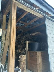 Fotografi av en utvendig struktur, sannsynligvis en uthus eller garasje, med en stabel vedvarende ved inni.