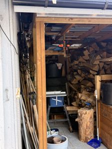 Fotografi av et utegårdsrom eller garasje med oppstilt ved, verktøy og utstyr.