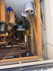 Fotografi av en uteplass eller garasje med oppstilt treverk, verktøy og ved.