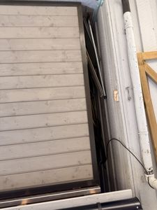 Fotografi av en del av en bygning, sannsynligvis en utvendig dør eller en del av fasaden med en hvit røype og en lys, panelert overflate.