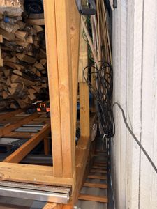 Fotografi av en utvendig vegg med tilhørende konstruksjon, hvor det er lagret vedvarende ved og en rullet kabel henger.