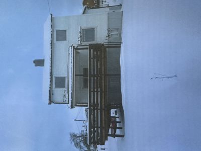 Fotografi av en hvit bygning med et utvendig tredekk, sett fra siden. Bygningen er omgitt av snø.