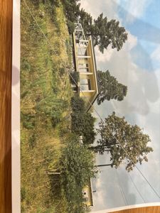 Fotografi av en moderne, gul bygning sett fra siden, omgitt av trær og vegetasjon.