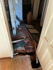 Fotografi av et rom i en bygning som er delvis ødelagt eller under renovering, med synlig skade på gulv og vegger.