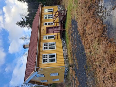 Fotografi av en gul farget bygning med rødt tak sett fra siden, med trapp opp til inngang.