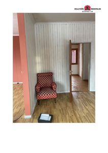 Fotografi av et rom i en bygning under ombygging eller renovering, med synlig gulv, panelvegger og en stol.