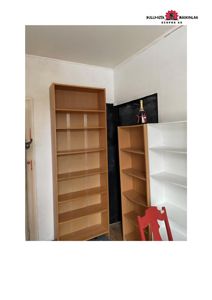 Fotografi av et rom inne i en bygning med bokhyller og en rød stol.