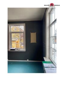 Fotografi av et rom i en bygning under ombygging eller renovering, med mørkegrå vegger, vinduer og gulv.