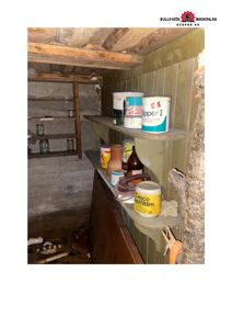 Fotografi av et innendørs rom, sannsynligvis en kjeller eller lagerrom, med hyller og byggematerialer.