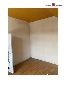 Fotografi av et tomt rom under eller etter renovering, med gulvpanel, gipsvegger og en åpen dør.