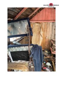 Fotografi av et gammelt, skadet interiør, sannsynligvis i en uthusbygning eller garasje, med møbler og gjenstander.