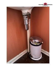 Fotografi av en vask undermontert i en hjørne, med synlige rør og en søppelkasse.