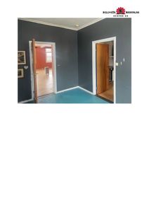 Fotografi av et rom med gråmalingde vegger, hvite lister og to dører som leder til andre rom.