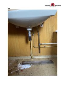 Fotografi av en vask undermontert i et bad, med synlige rør og en gulvrenne.