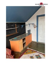 Fotografi av et innendørs rom med skrivebord, hyller og en dør.