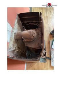 Fotografi av en rustet ventilasjonsanlegg (kanskje en gyllepumpe eller lignende) som er montert i et hull i veggen.