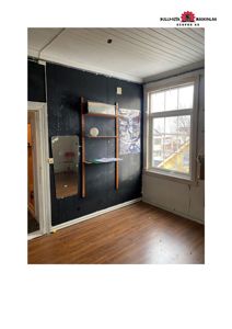 Fotografi av et innvendig rom i en bygning, sannsynligvis under renovering eller etter riving, med mørke panelvegger og gulv.