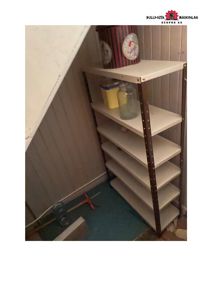 Fotografi av et hjørne i et rom, sannsynligvis et underetasje eller kjeller, med en metallhylle og en skrått tak.