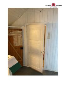 Fotografi av en hvit dør i et rom med hvite panelvegger og en skrå taklinning.