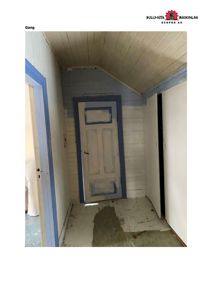 Fotografi av en gang i et hus under renovering eller etter skade, med synlig vannskade på gulvet og delvis maling.