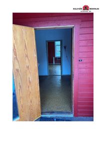 Fotografi av en døråpning i en rød bygning som leder inn i et rom med blåmaling og gulv.