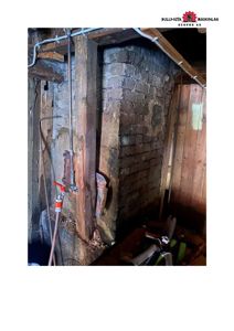 Fotografi av en gammel, steinmur med vedvokst trekonstruksjon og rør i et underjordisk eller kullrom.