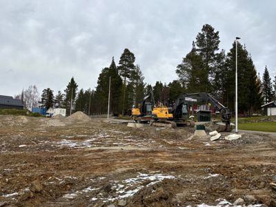 Fotografi av et byggefelt under utgravning med graver, maskiner og omgivende natur.
