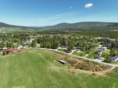 Luftfoto av et boligområde med en stor, grønn tomt i forgrunnen. Bildet viser eksisterende bebyggelse, veier og natur.