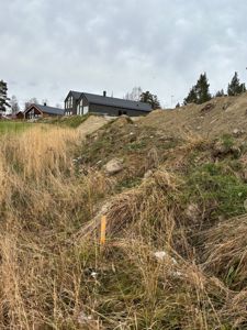 Fotografi av et tomteområde med grøfting og en bygning i bakgrunnen.