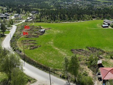 Luftfoto av et grønt felt med skog og bebyggelse i bakgrunnen. Bildet viser to markerte områder med røde bokstaver 'B4' og 'B5', som antageligvis er tomtegrunnlegger eller planlagte byggeplasser.
