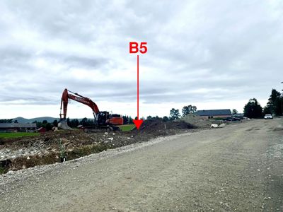 Fotografi av et byggefelt med graving, en excavator og en vei i bakgrunnen.