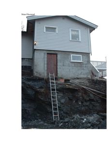 Fotografi av en eksisterende eller under oppføring bolighus med grå fasade, betongfundament og en trapp opp til en terrasse.