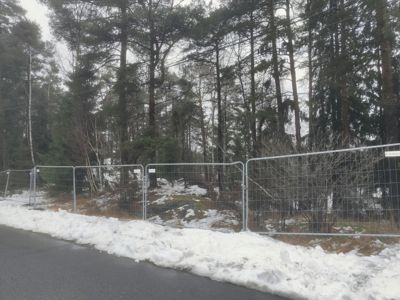 Fotografi av en vei med snø ved siden av, en midlertidig hekk og en skogbakgrunn.