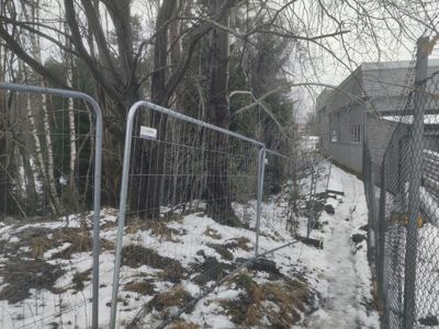 Fotografi av en bygning sett fra siden, med en snødekt sti og en midlertidig hekk i forgrunnen.